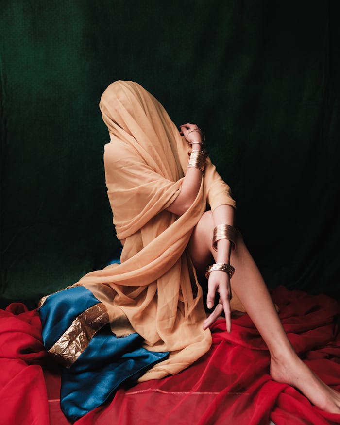 An artistic portrait of a model draped in vibrant fabrics and metallic jewelry, evoking a sense of mystery and elegance.